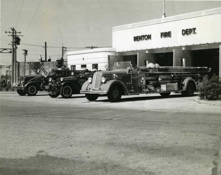 Black and white image of three fire trucks parked in front of the an art deco-style building, with letters on the facade that read "Renton Fire Dept."