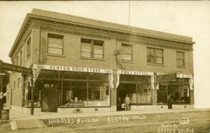 Sepia image of a two story brick building with sashes over the windows reading "Renton Drug Store" and "Post Office". On the second story, letters on the windows read "Dentist". Four men and one child pose in the entry ways.