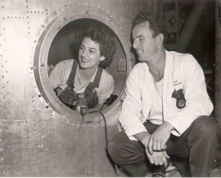 Black and white image of a man and woman working on a part of an airplane