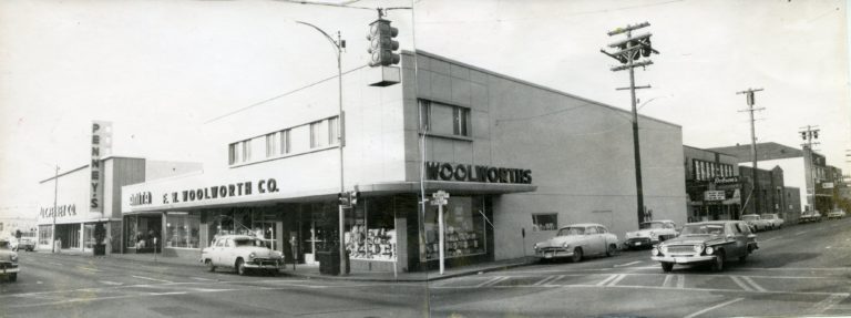 Black and white image of the two-story F.W. Woolworth Co. building, taken from the street intersection, with cars driving