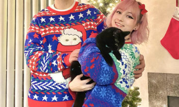 A man and woman in holiday garb pose for a photo while holding a cat.