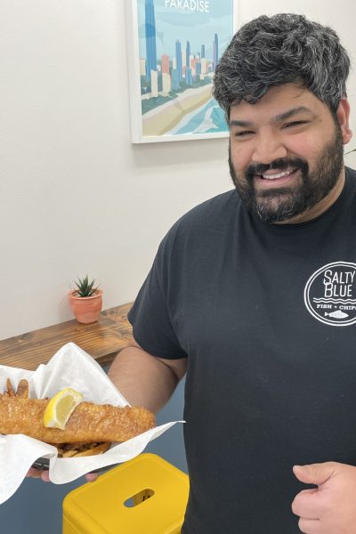 man holding fish and chips with a half blue wall and posters behind him.